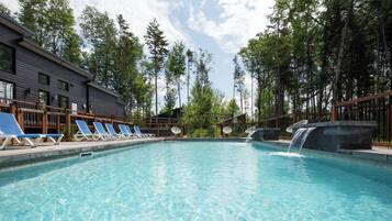 Ein Swimmingpool mit Liegestühlen, einem Wasserfall und einem Gebäude mit dunkler Fassade.