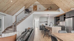 Eine moderne Küche mit einer zentralen Kochinsel, einem Essbereich mit einem Holztisch und einer Treppe, die zu einer oberen Ebene führt.