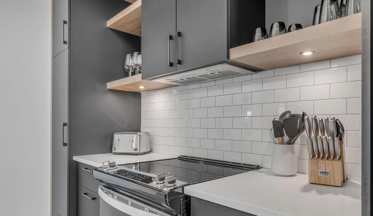 A modern kitchen with grey cabinets, a white countertop, a built-in oven, a toaster, and a knife block.