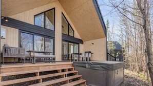 Ein modernes Holzgebäude mit großen Fenstern, Außenbestuhlung und einem Whirlpool.