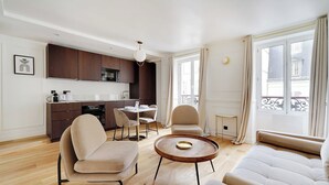 Ein modernes Wohnzimmer mit einer Couch, Sesseln, einem Couchtisch und einer Küchenzeile inklusive Schränken und einem Esstisch.