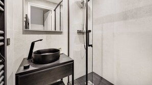 Ein modernes Badezimmer mit einem schwarzen Waschbecken, einem Spiegel und einer Duschkabine aus Glas.