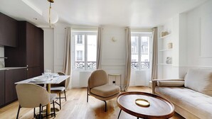 Ein modernes Wohnzimmer mit einer Couch, einem Esstisch mit Stühlen, einem runden Couchtisch und einer Küchenzeile mit Schränken und einem Fenster.