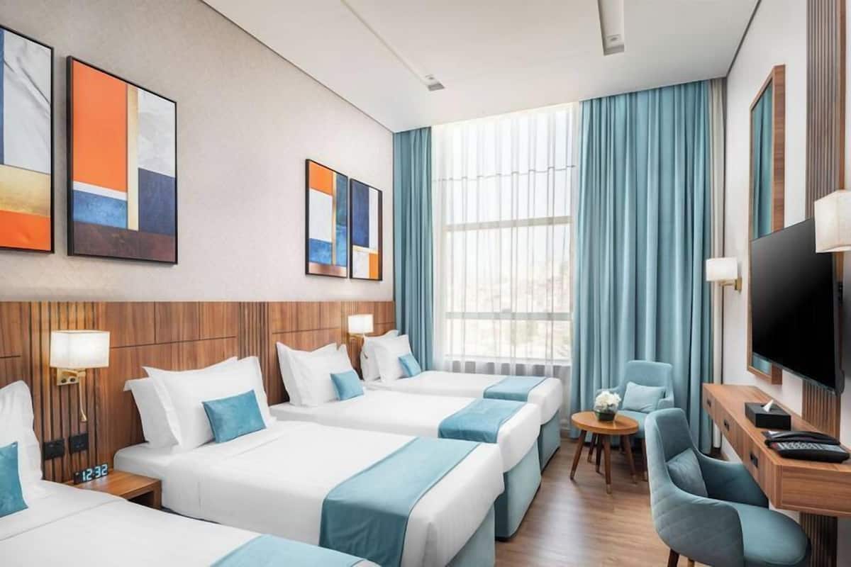 A hotel room with three beds, a desk with a TV, and artwork on the walls.