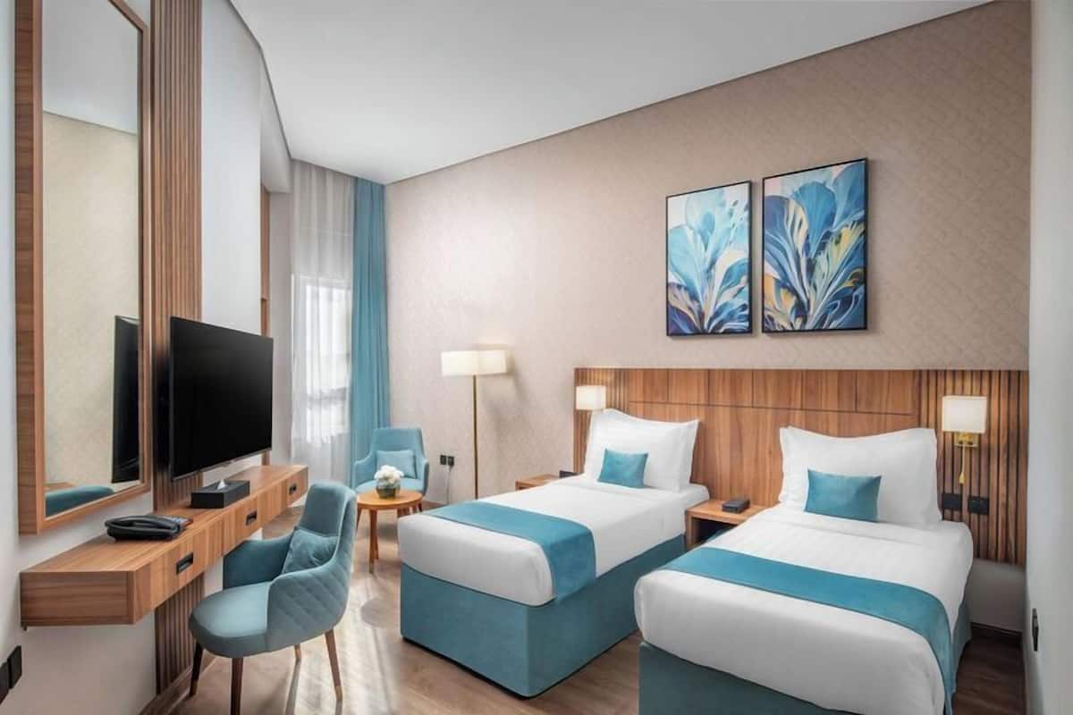 A hotel room with two beds, a TV, a desk, and a chair.