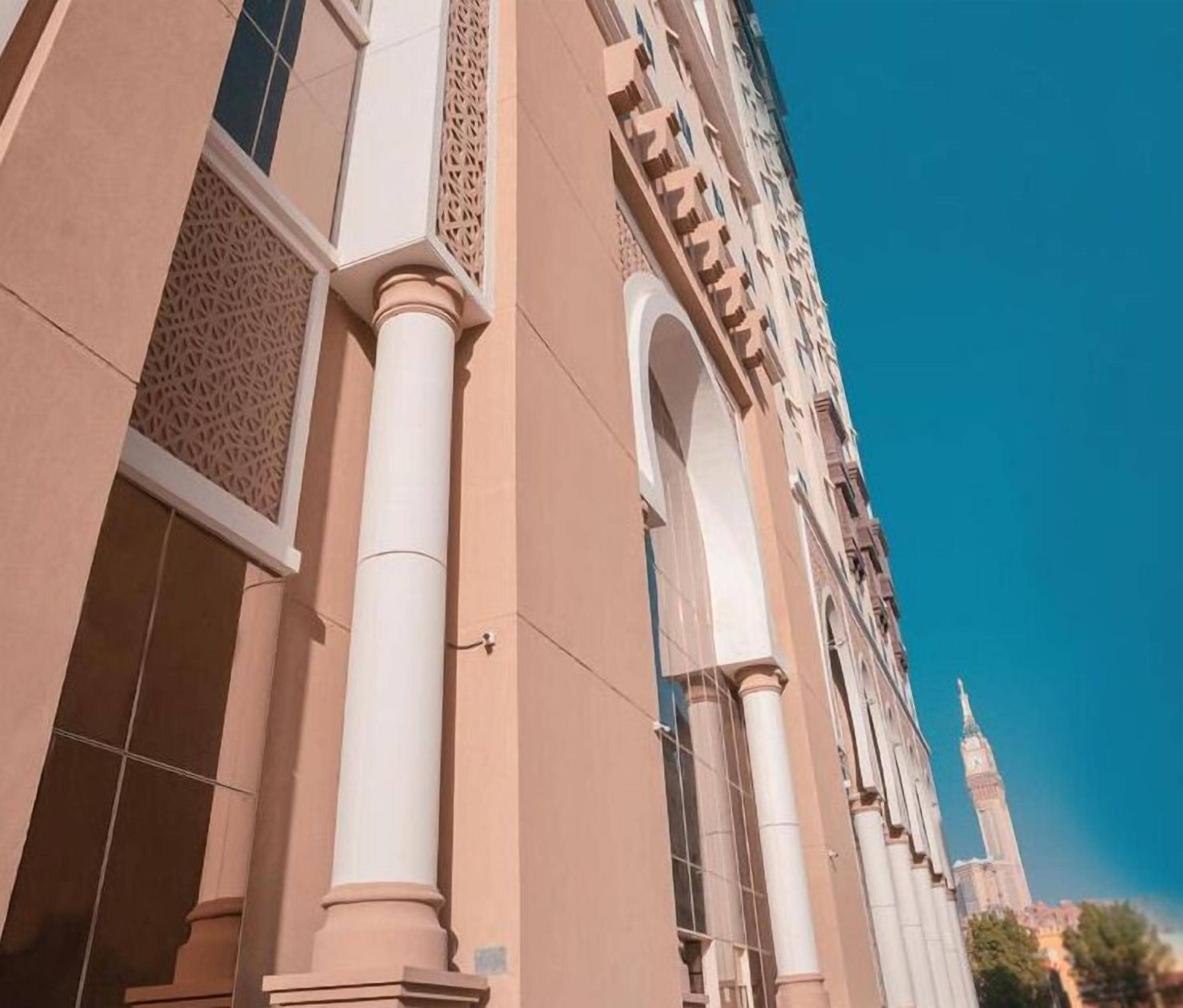 A building with large columns and arched windows, featuring intricate lattice work and a clear view of a tower in the background.