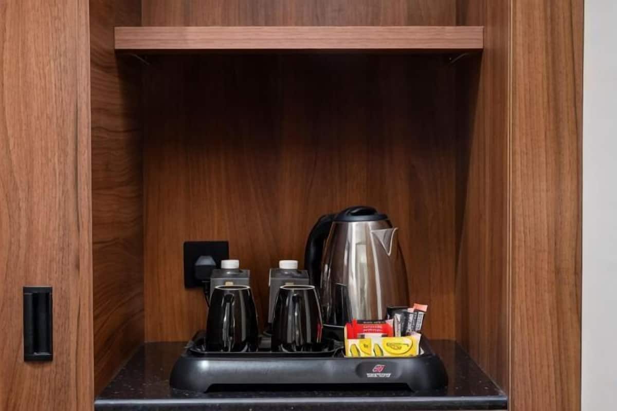 A wooden cabinet with a coffee maker, two cups, a kettle, and a box of tissues.