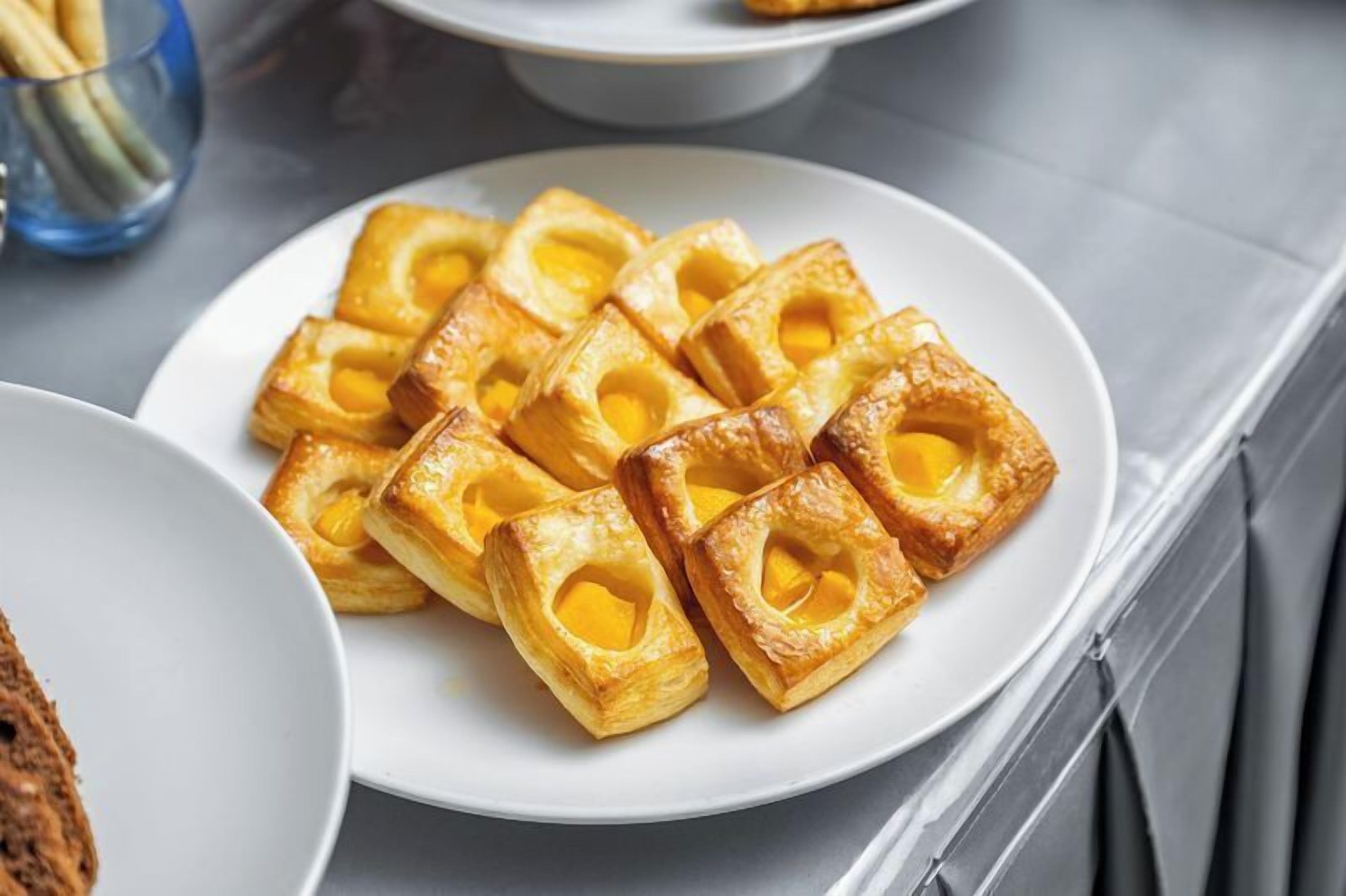 A plate of square pastries with a golden-brown crust and a yellow filling, arranged on a white plate.