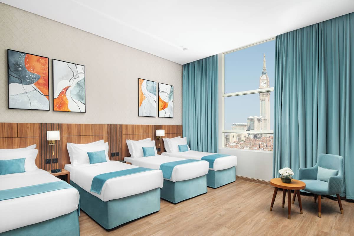 A hotel room with four beds, a view of a tower, and artwork on the wall.