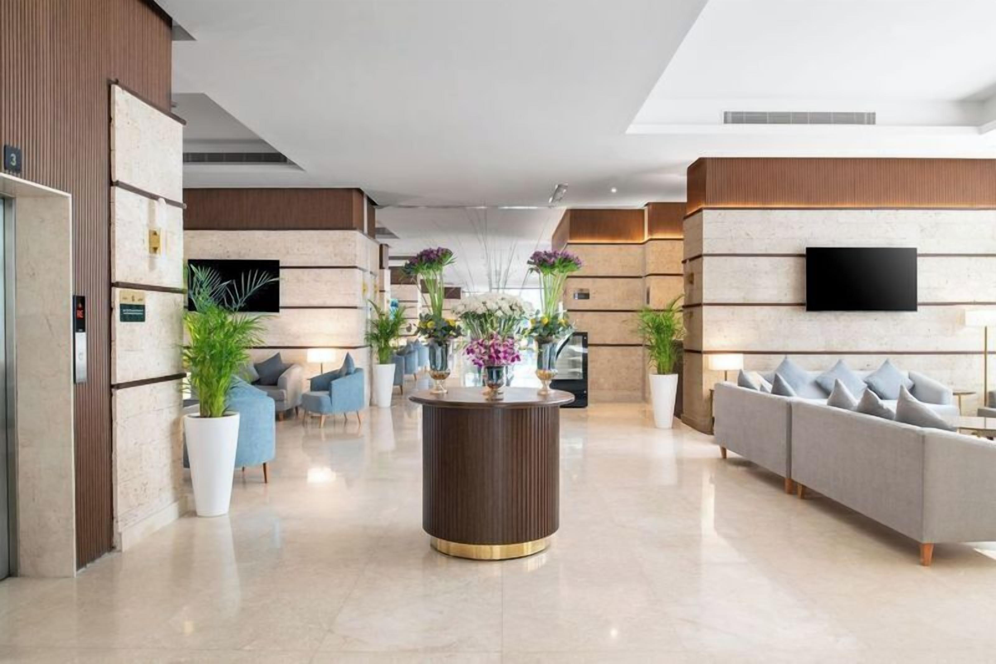 A modern lobby with a central round table, seating area, and a flat-screen TV mounted on the wall.