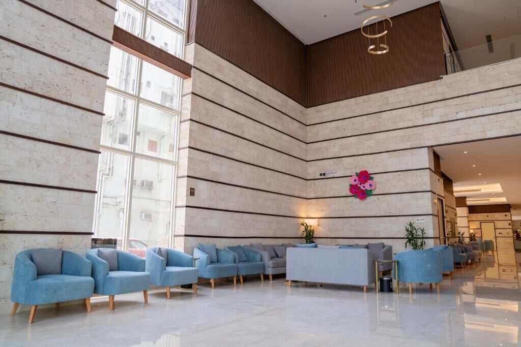 Een ruime lobby met een hoog plafond, een centraal zitgedeelte met banken, en een groot raam dat natuurlijk licht binnenlaat.