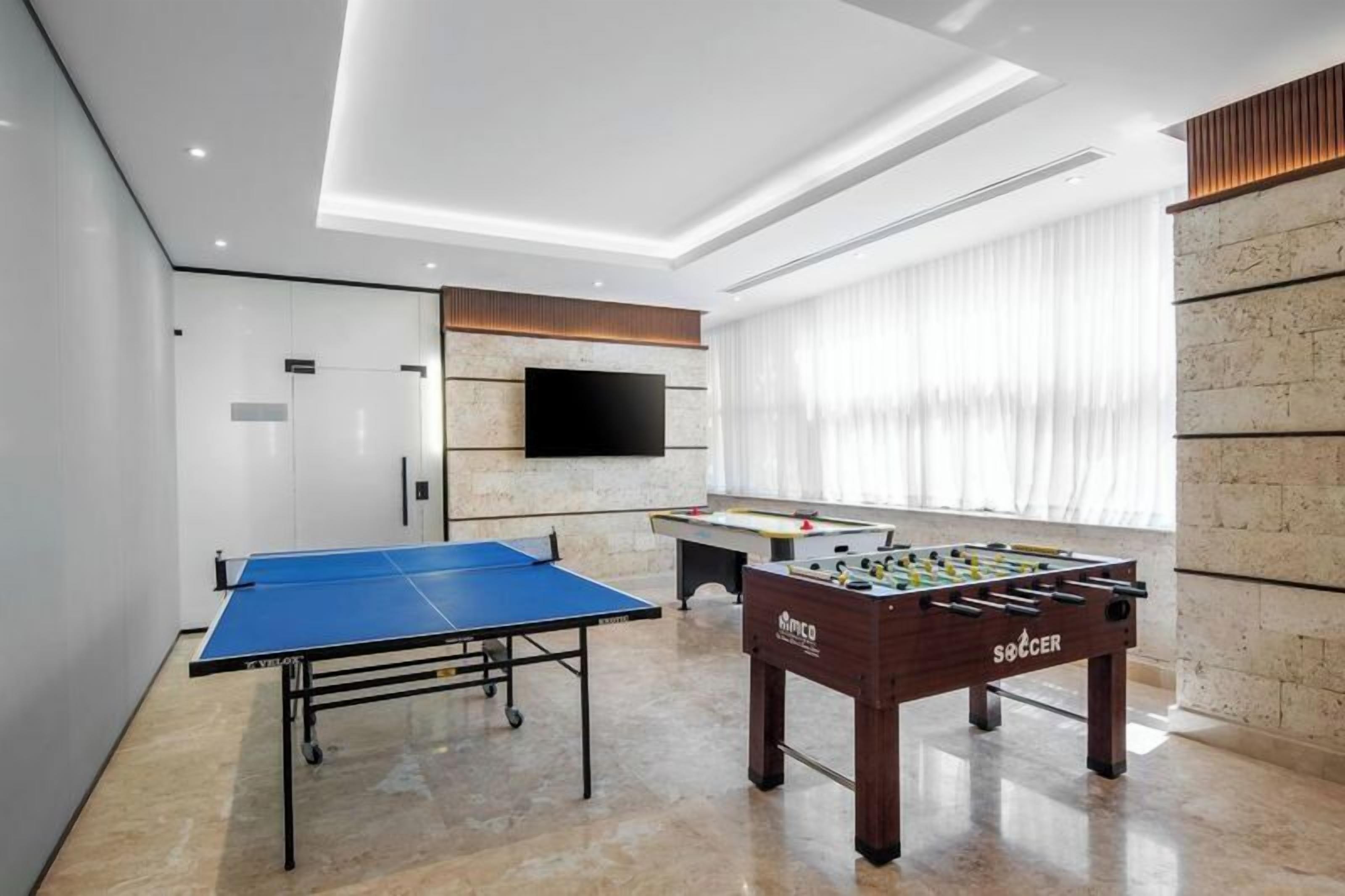 Quarto moderno com mesa de pingue-pongue, mesa de futebol de mesa e televisão de tela plana na parede.