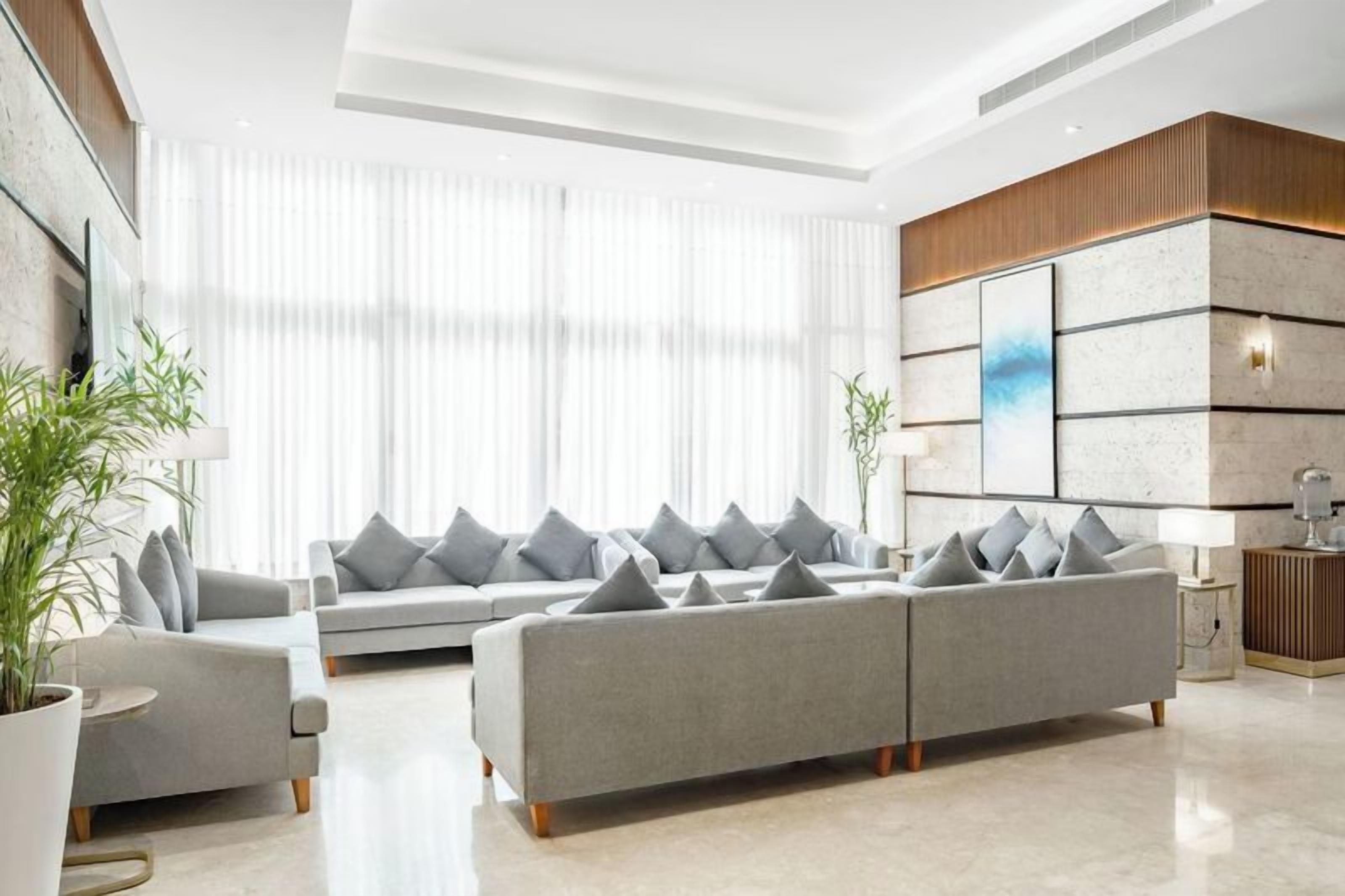 A modern living room with a grey sofa set, a large window with sheer curtains, and a minimalist decor.