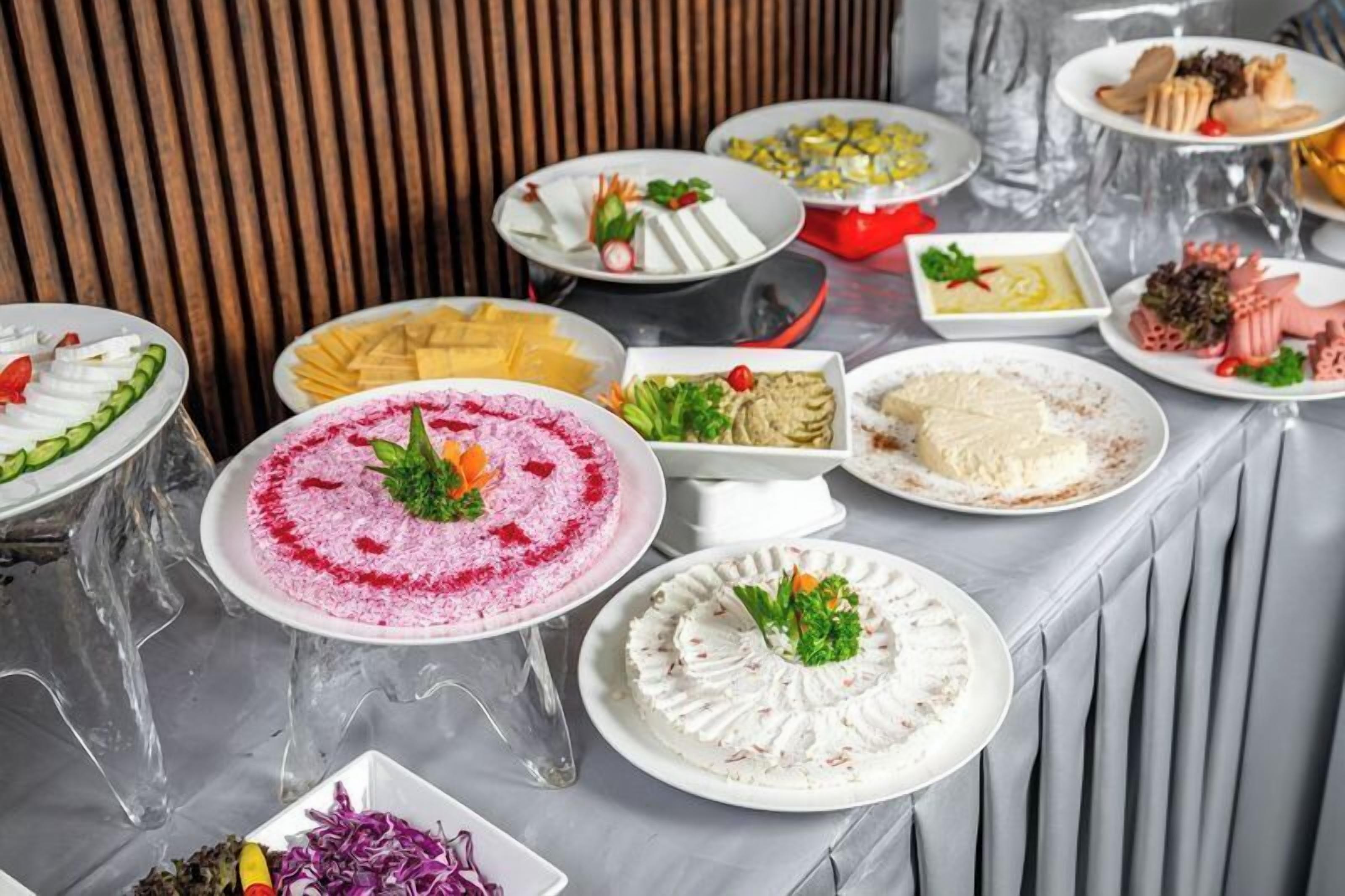 Ein reichhaltiges Buffet mit verschiedenen Speisen, darunter ein pinkes Dessert, weiße Cremes und weitere Gerichte.