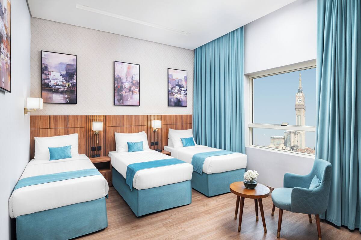 A hotel room with two beds, a chair, a small table, and a window with a cityscape view.
