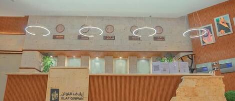 A reception area with a sign indicating 'Opening soon'. There are nameplates above a counter, a wooden reception desk, and a large rock-like structure to the right.