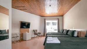 A hotel room with a wooden ceiling, a television, a desk, a chair, and two beds with green bedding.