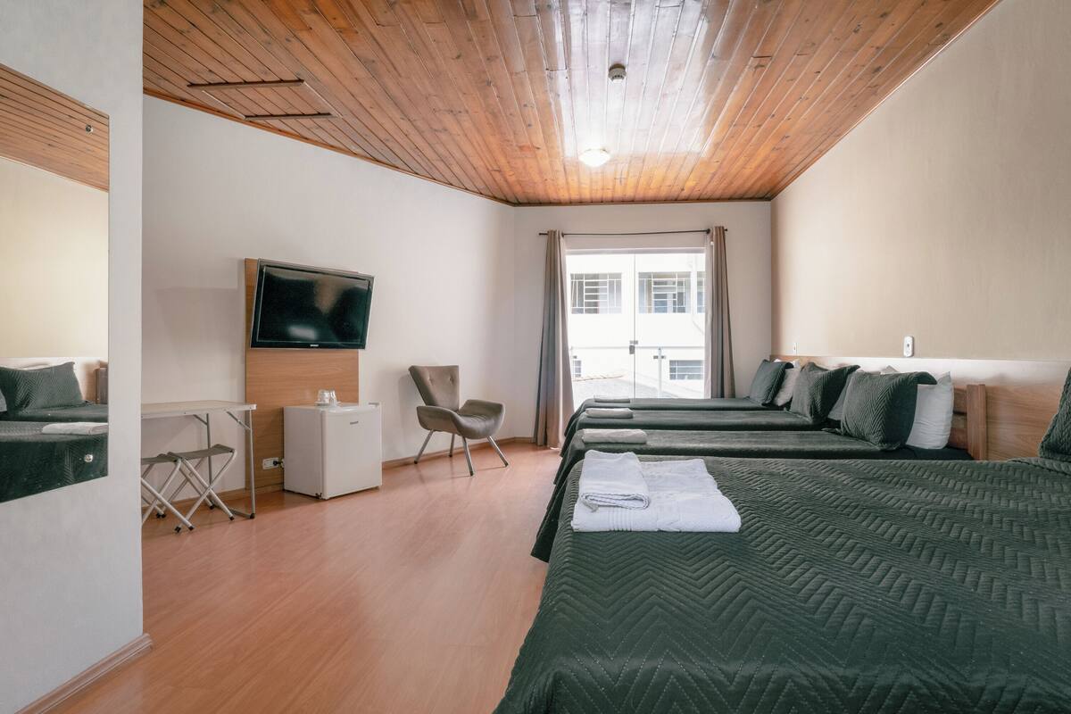 Habitación de hotel con techo de madera, televisor, escritorio, una silla y dos camas con ropa de cama verde.