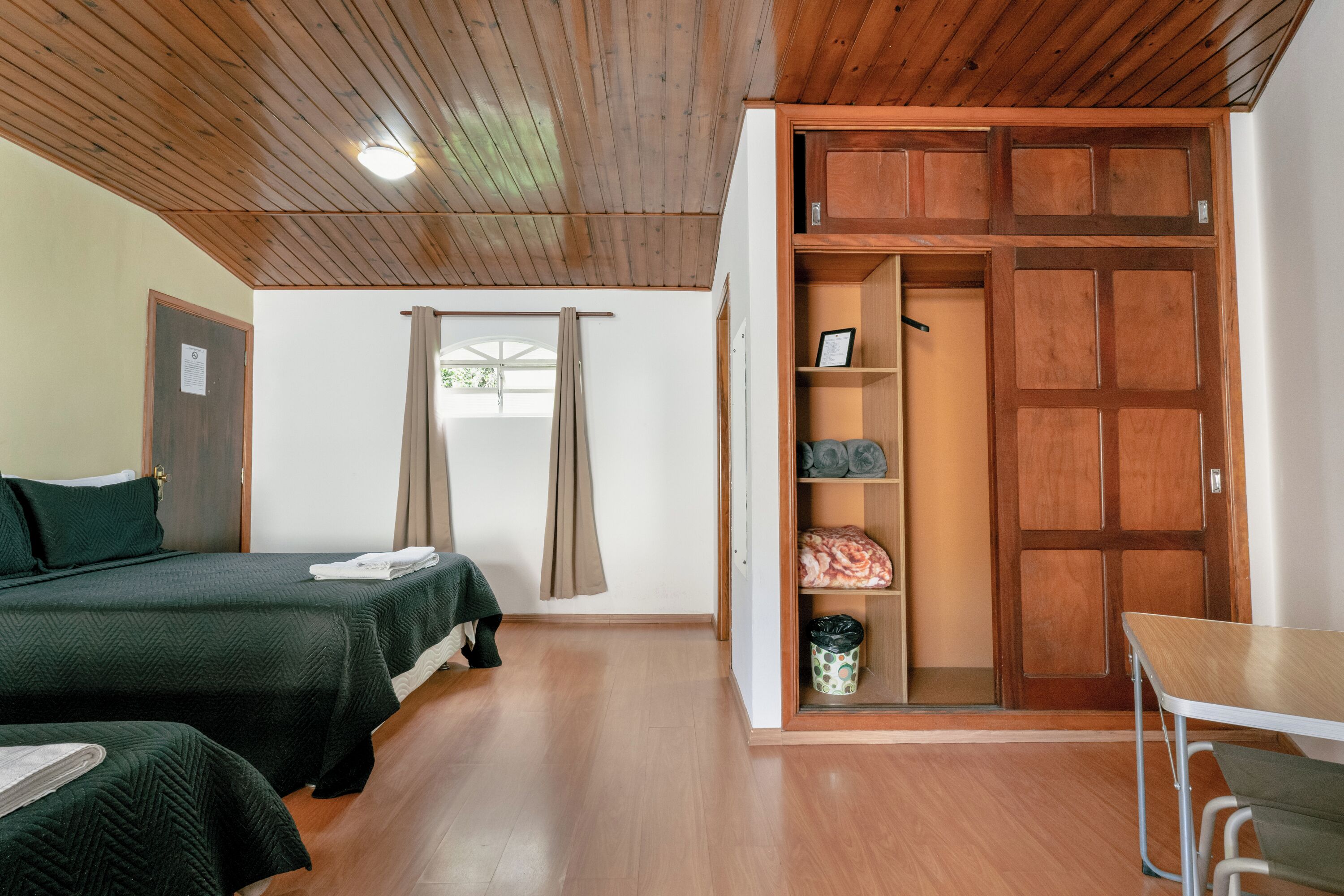 A room with two beds, a wooden wardrobe, a table, and a window with curtains.