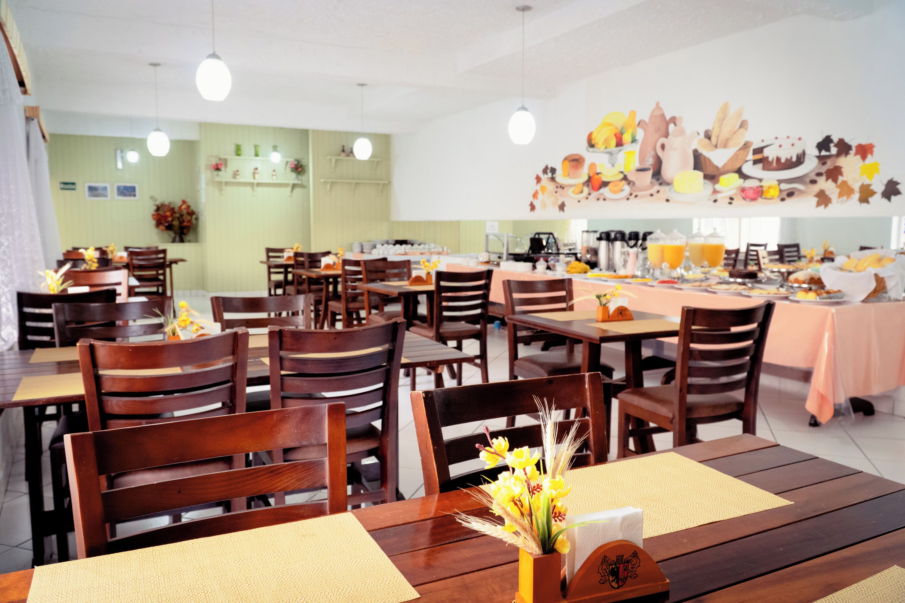 A restaurant with wooden tables and chairs, a buffet setup, and a wall decorated with food illustrations.