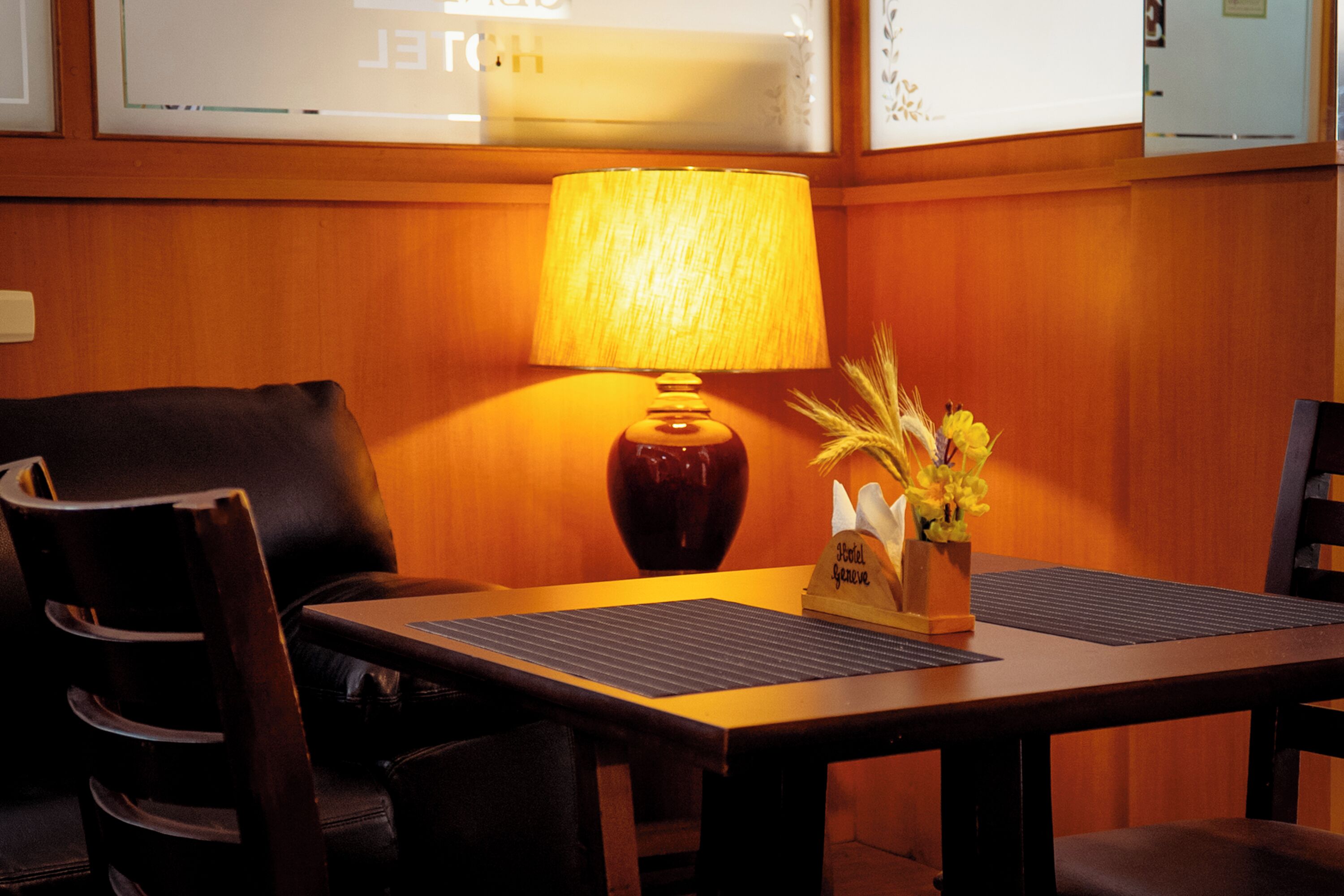 A hotel room with a wooden paneled wall, a table with a lamp, a vase with flowers, and a sign that reads "Total Spa."