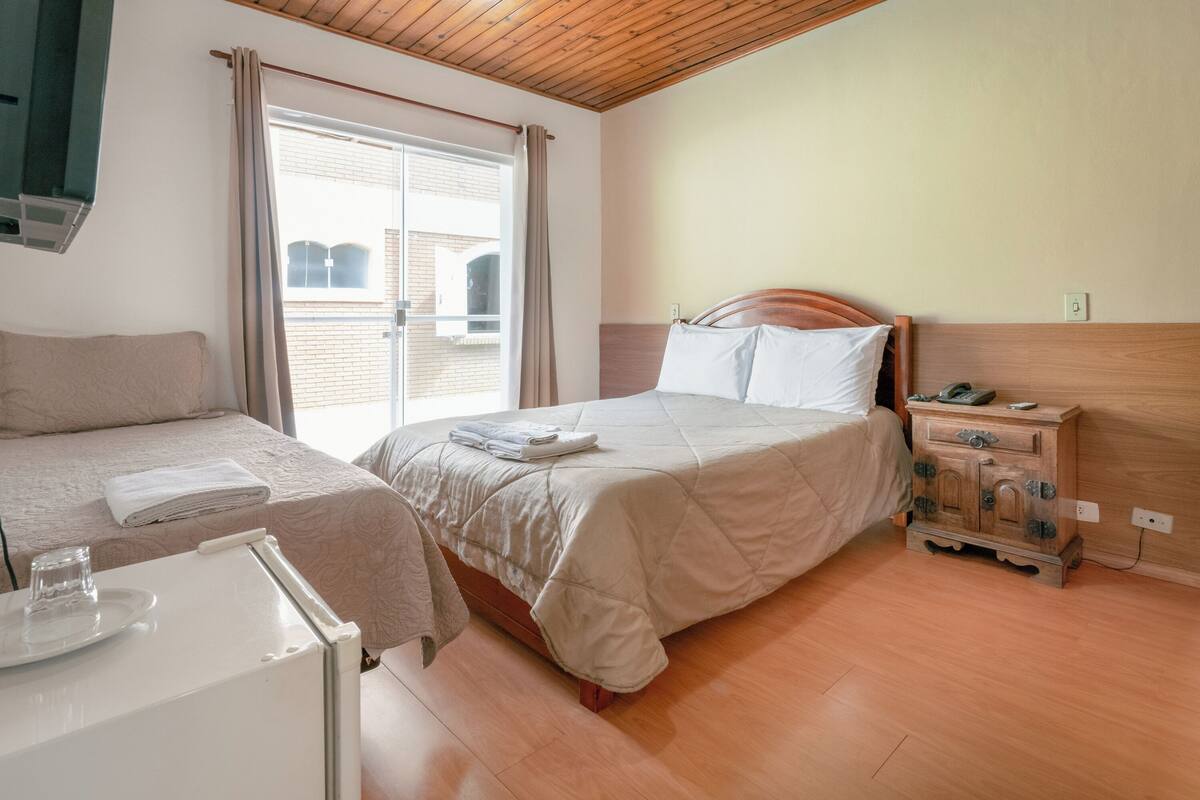 Un dormitorio con dos camas, un aparador de madera, una mesita con un vaso y una ventana con cortinas.