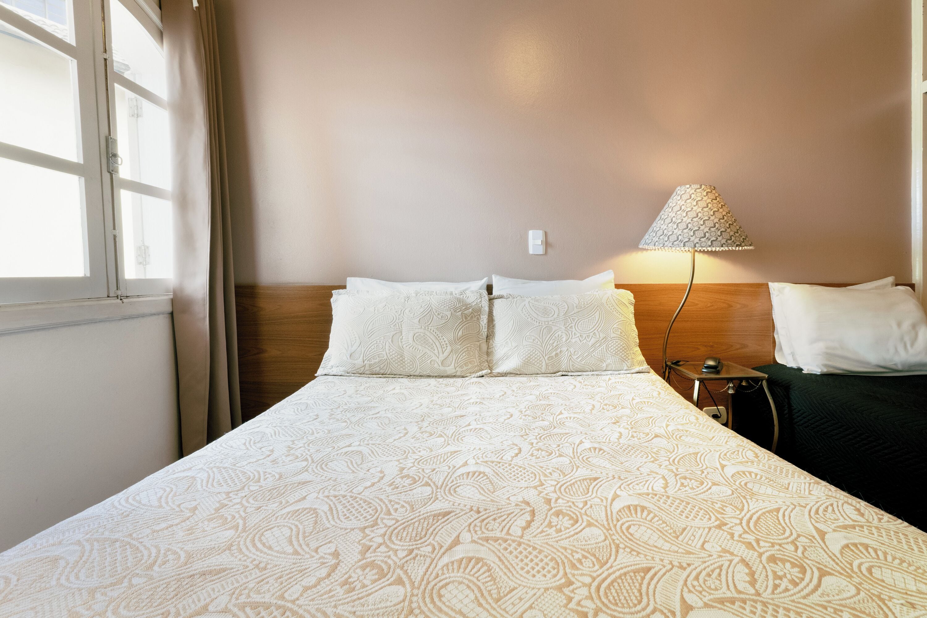 Una cama bien hecha con una colcha estampada, una lámpara de noche y una mesita de noche con un teléfono.
