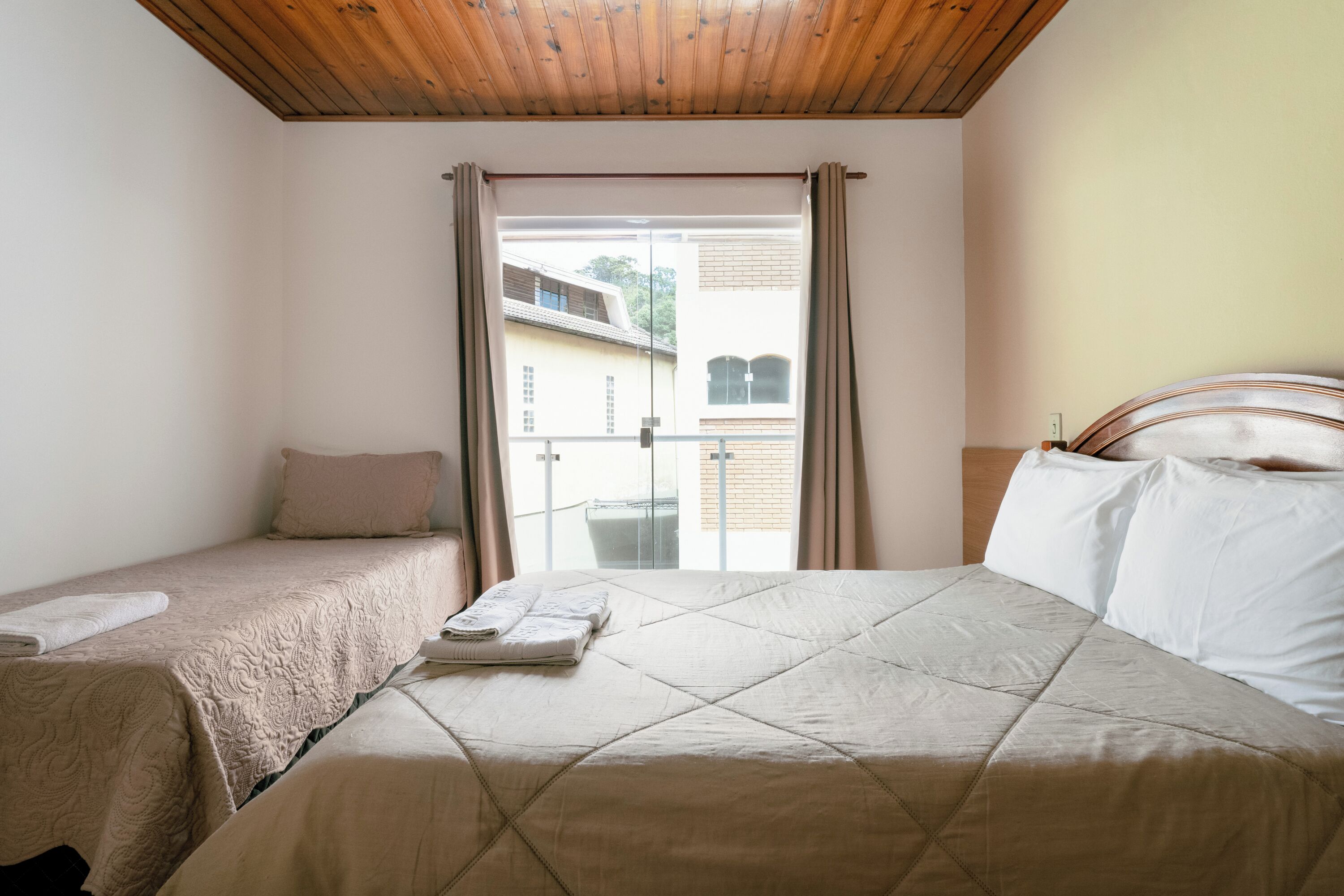 A bedroom with two beds, a balcony, and a wooden ceiling.
