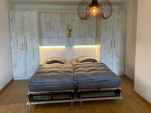 A bed with a headboard, bedside tables, and a hanging light fixture. - Apartment with great view in a 4* hotel with Pool, Sauna and Fitness (Beatenberg)