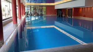Una amplia piscina interior con agua cristalina, rodeada de pilares rojos y paredes de vidrio.