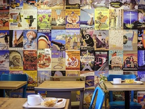 Un mur recouvert d’anciennes affiches de voyage, avec une table et des chaises au premier plan.