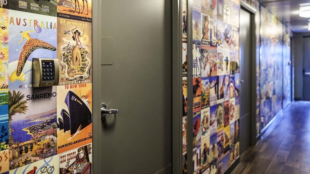 A hallway with travel posters on the walls, a door, and a wooden floor.