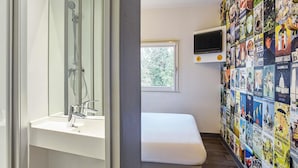 A bathroom with a shower, a sink, a bed, and a wall with travel posters. - Hotelf1 Marseille Plan De Campagne N°1 (Rénové) (Les Pennes-Mirabeau)