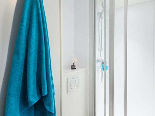 A bathroom with a glass shower enclosure, a towel rack with a blue towel, and a small shelf with toiletries.