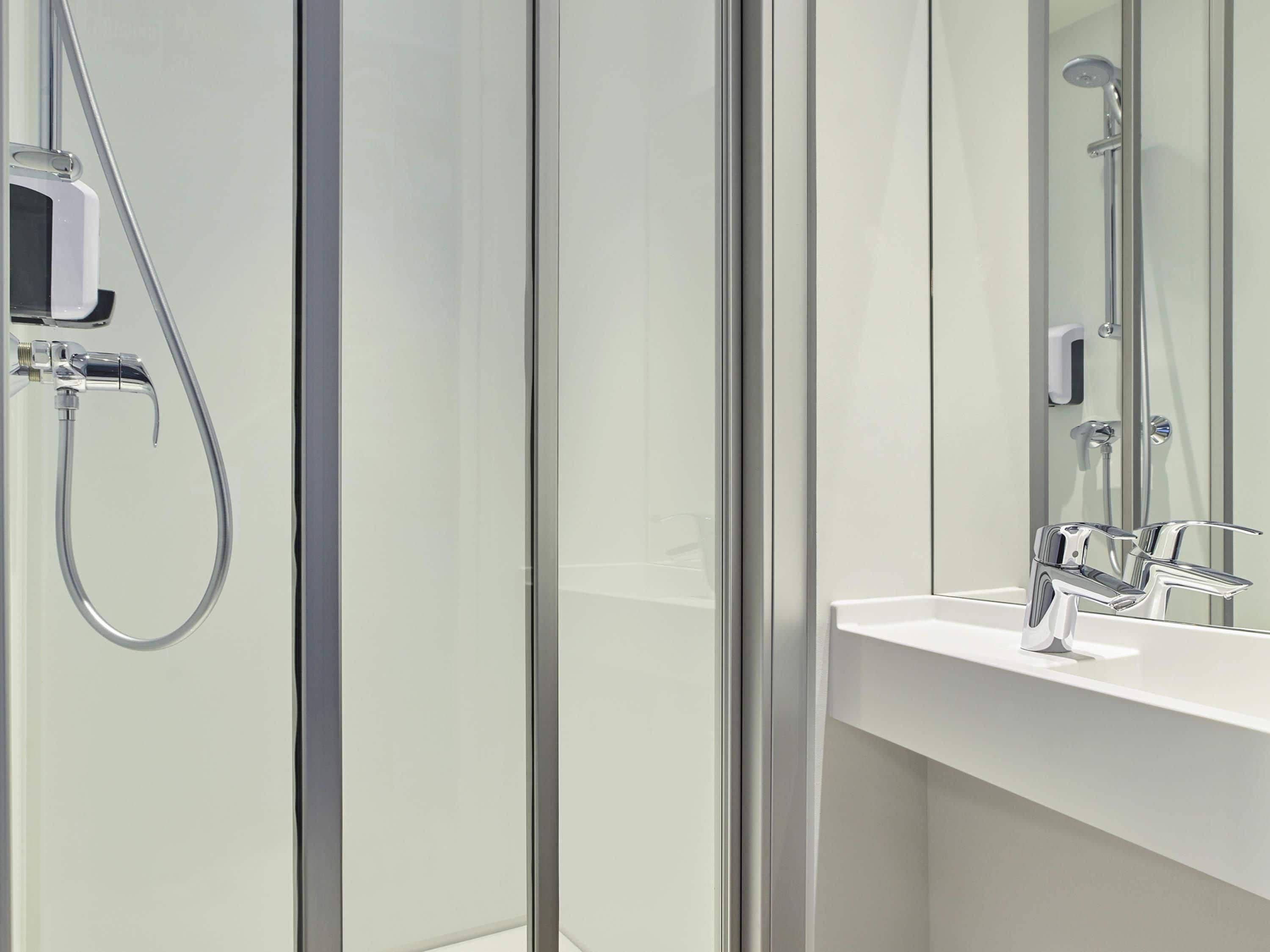 Un baño moderno con cabina de ducha de vidrio, un lavabo blanco y un espejo.