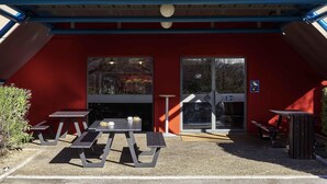 A hotel entrance with a red exterior, a yellow sign reading 'hotelFL.com', and a covered outdoor seating area with tables and benches.
