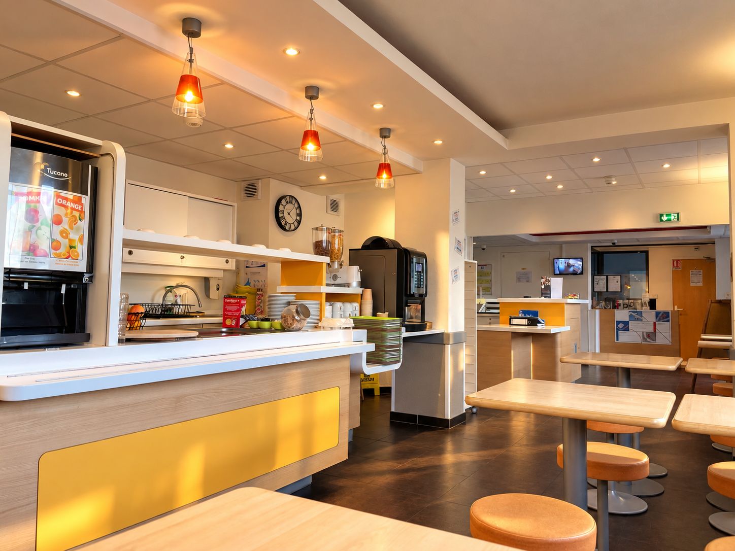 Un interior de cafetería moderna con mostrador, zona de asientos y un reloj en la pared.