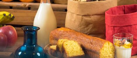 A loaf of bread, a glass of milk, and a bowl of fruits and nuts on a wooden table.