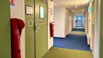 A hotel corridor with doors numbered 2 and 3, fire extinguishers, and emergency exit signs.