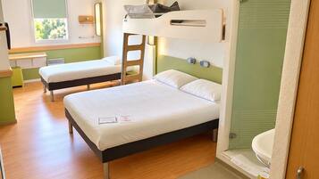 A hotel room with two single beds, a bunk bed, a small desk, a window, and a bathroom.