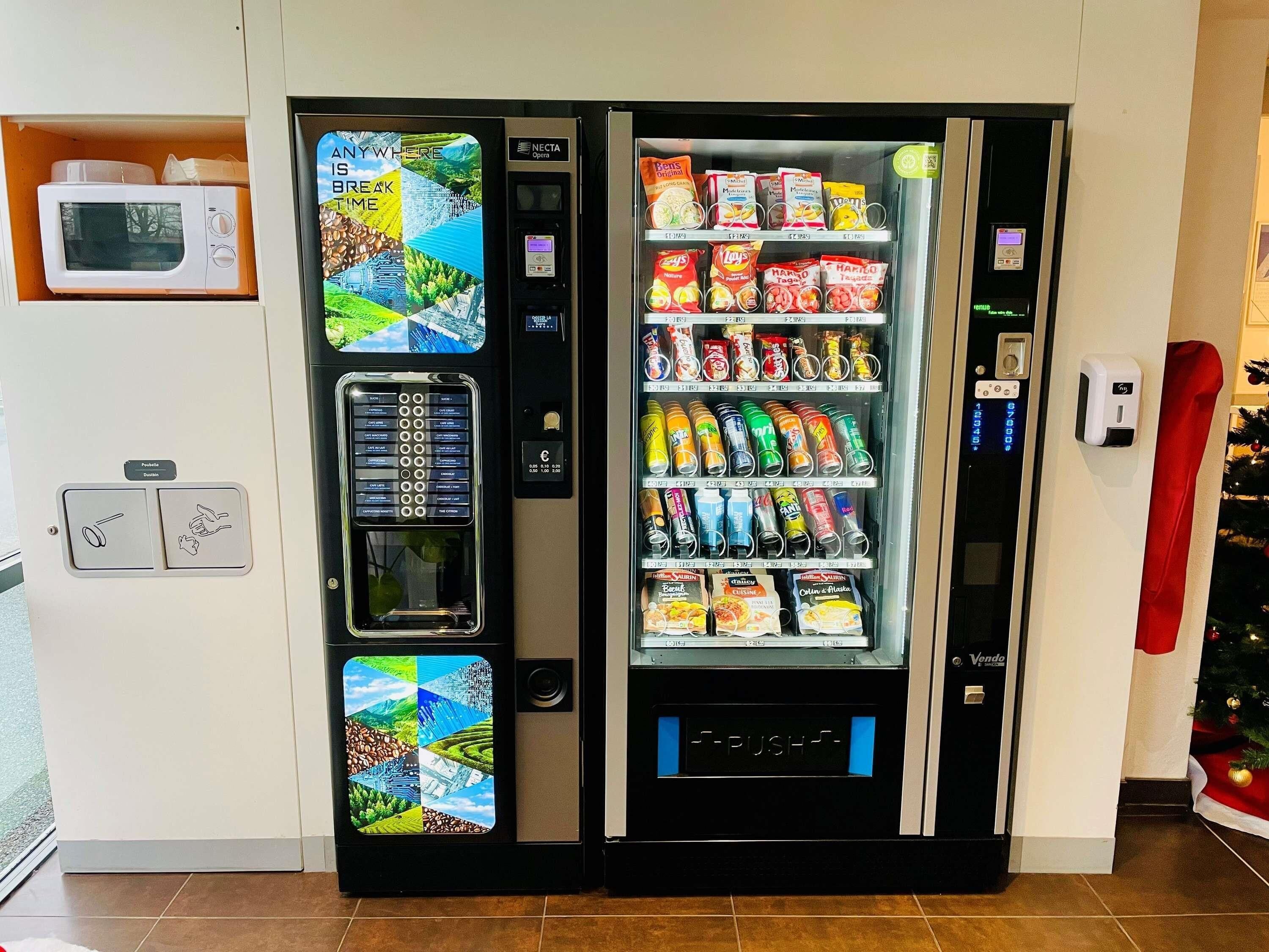 Ein Getränkeautomat mit verschiedenen Snacks und Getränken, einer Mikrowelle und einem Bezahlsystem.