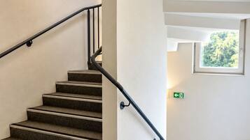 A staircase with a handrail, carpeted steps, and a window with a view of trees.