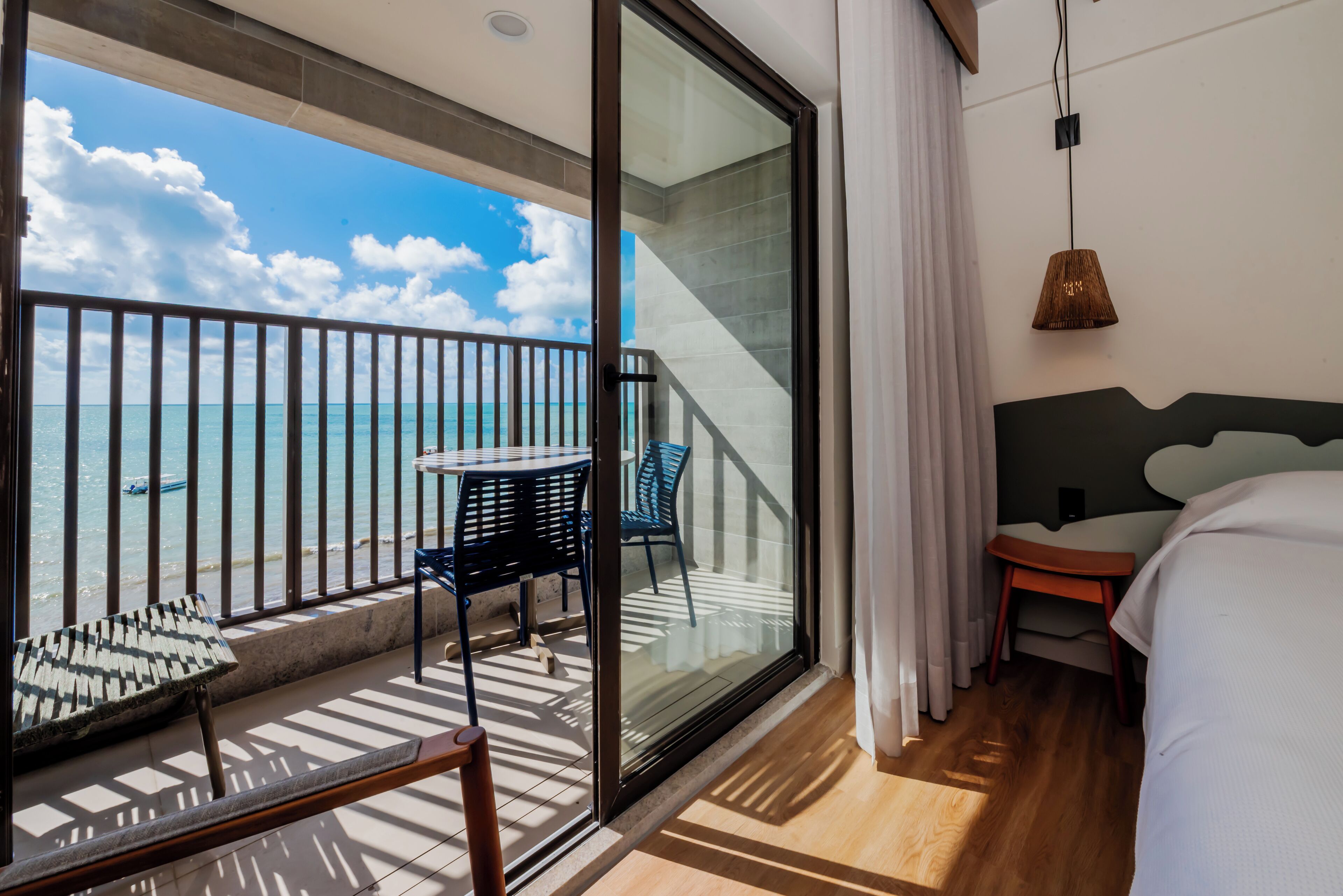 Un balcón con vista al mar, una mesa, sillas y una cama con cabecera.