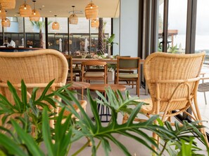 Un restaurante con mobiliario de mimbre, ventanas amplias y plantas de interior.