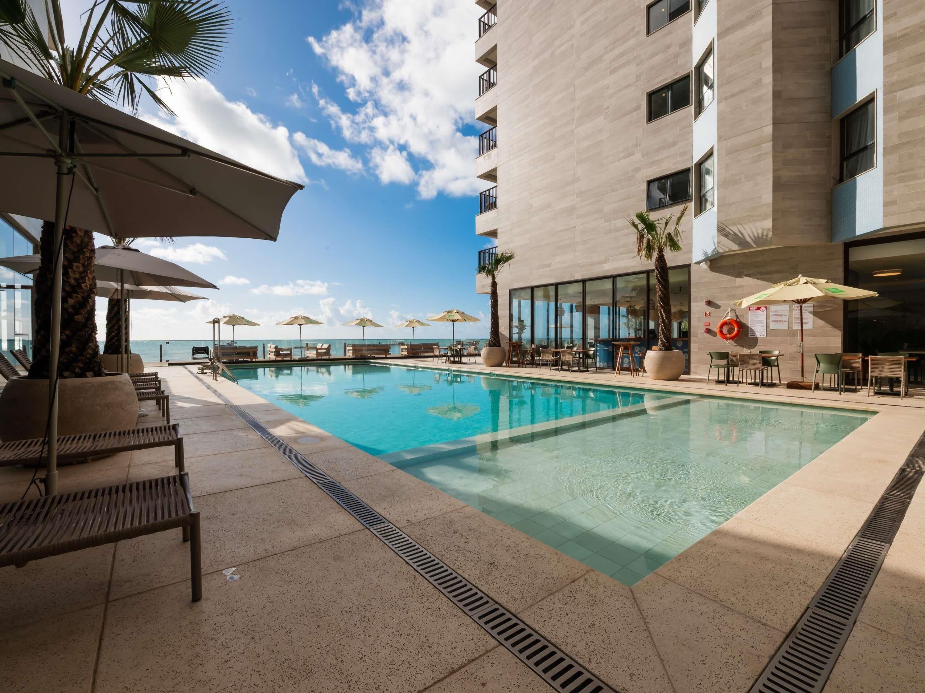 A pool area with lounge chairs, umbrellas, and a view of the ocean.