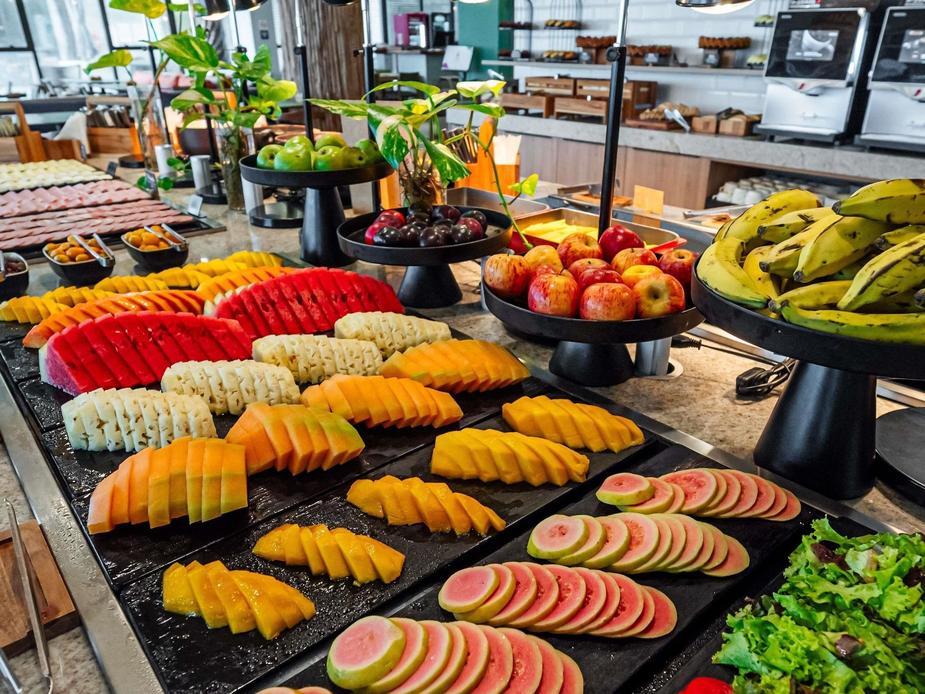 Un bufé con diversas frutas y verduras dispuestas ordenadamente en bandejas.