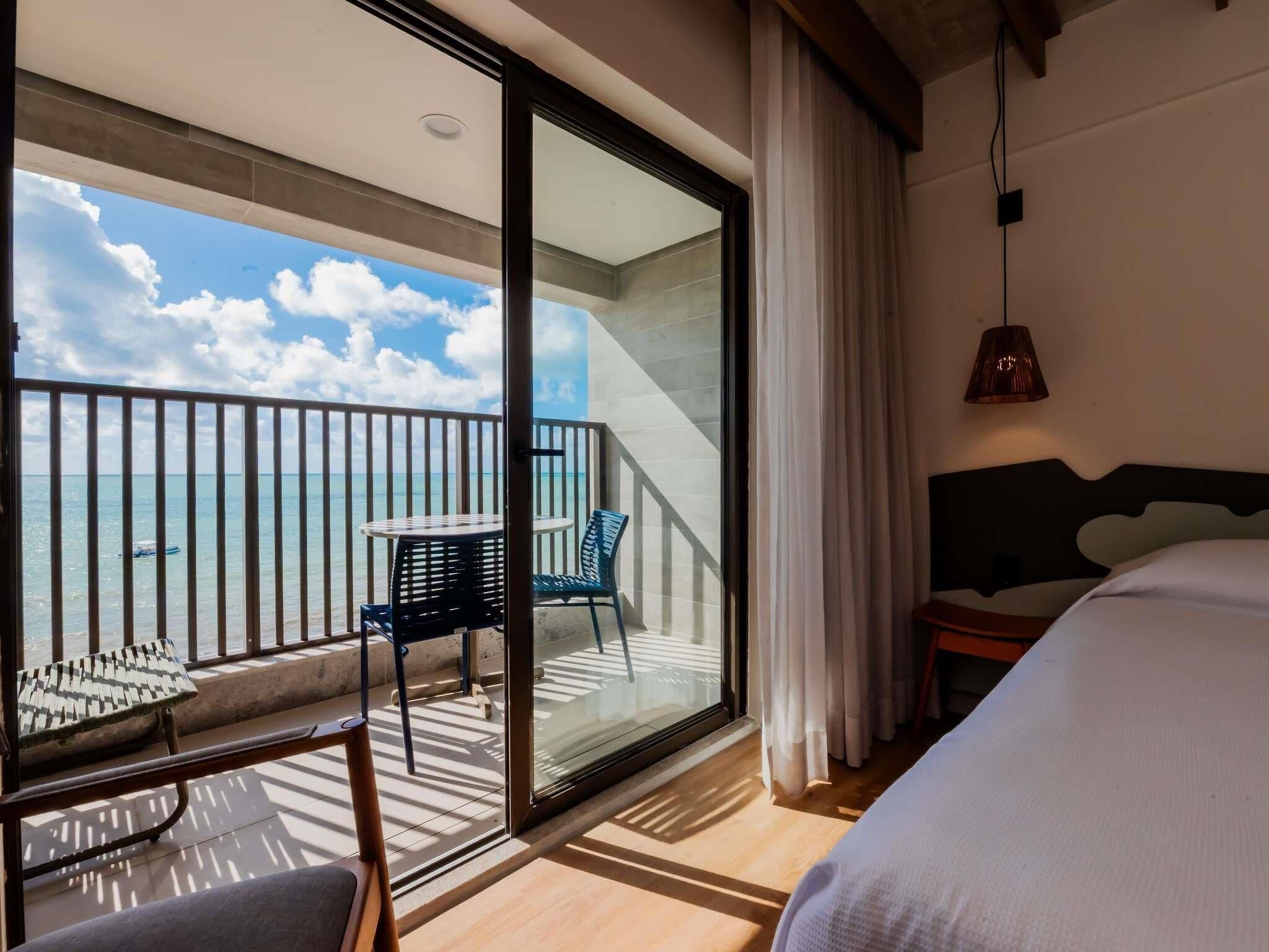 A hotel room with a balcony, a bed, a table, and two chairs.