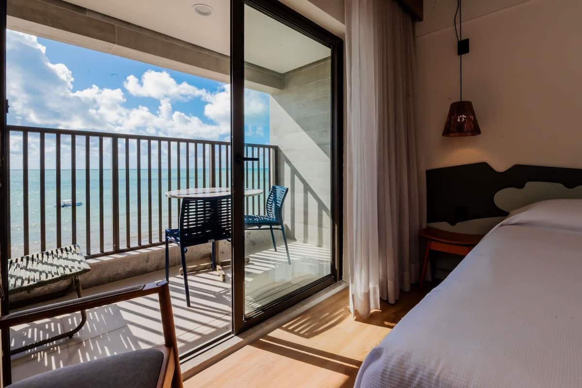 A hotel room with a balcony, a bed, a table, and two chairs.