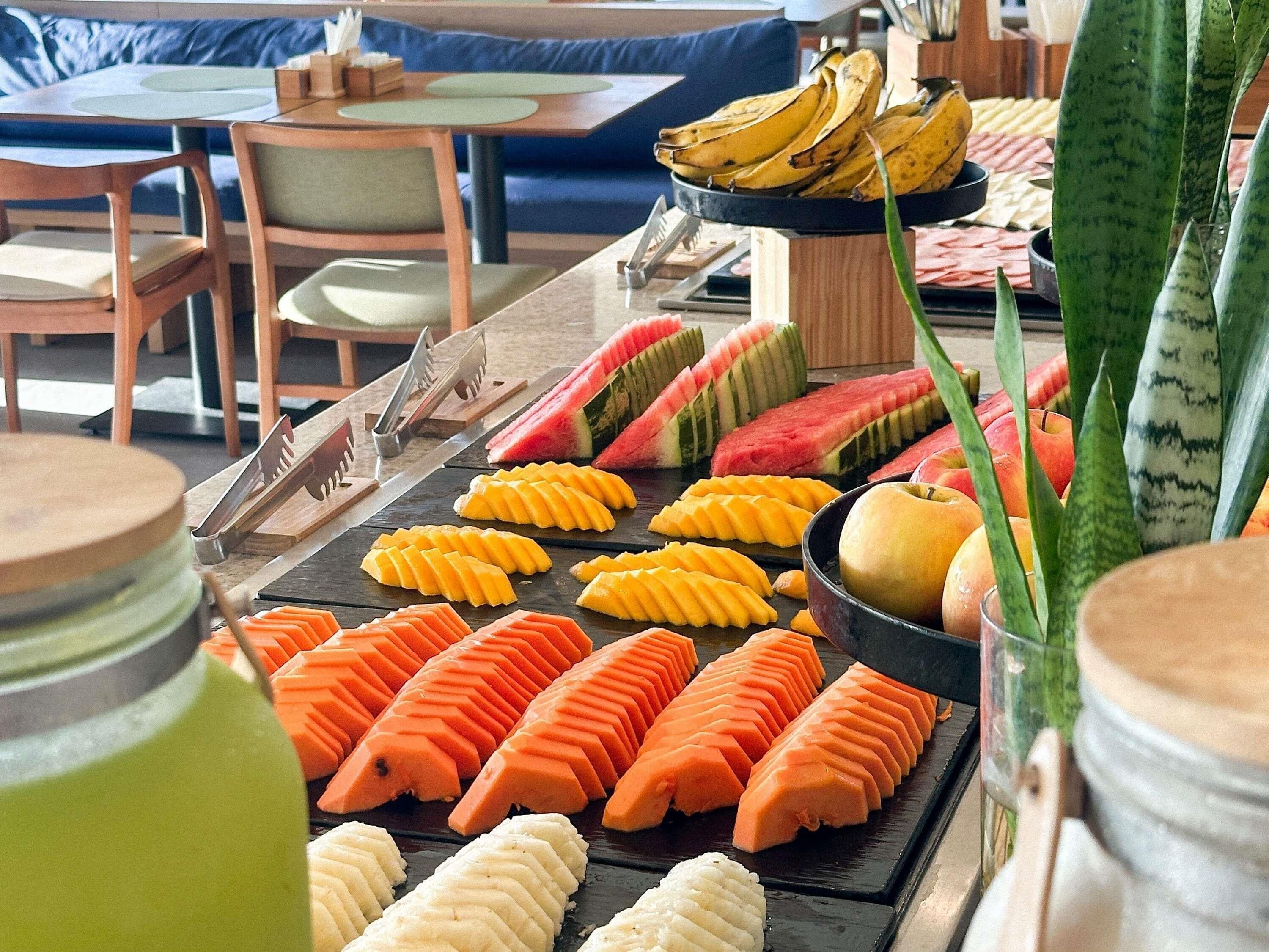 A buffet with sliced fruits and vegetables, a bowl of bananas, and a potted plant.