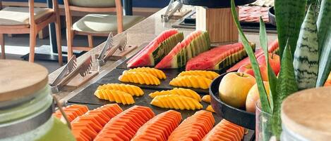 A buffet with sliced fruits and vegetables, a bowl of bananas, and a potted plant.